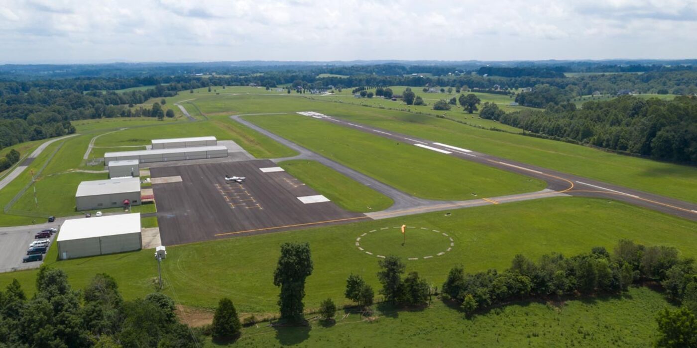 Aerial view of Russell County Airport: the ramp and hangar row on the left, the segmented circle and windsock beside the runway, farmland beyond.